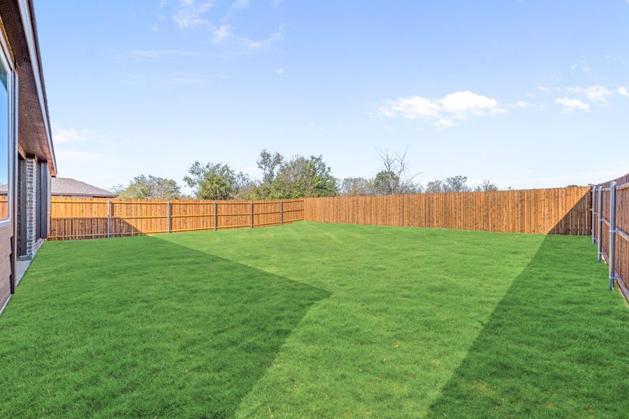 Spacious backyard with green grass lawn and full wood privacy fence surrounding the yard