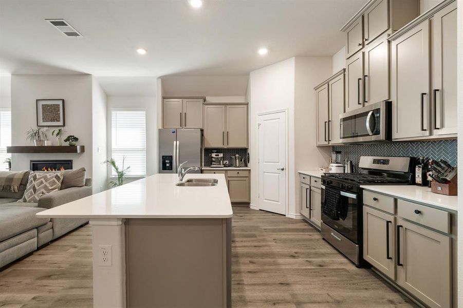 Kitchen featuring stainless steel appliances, open floor plan, tasteful backsplash, a kitchen island with sink, and light wood-style flooring Kitchen featuring stainless steel appliances, open floor plan, tasteful backsplash, a kitchen island with sink, and light wood-style flooring