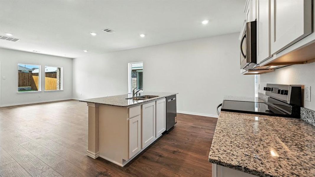 Open-concept kitchen featuring an island with a stainless steel sink, granite countertops, wood-finish flooring, white cabinetry, and recessed lighting