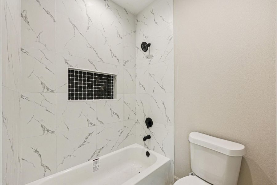 Modern tub and shower with black shower head. A built-in niche with dark mosaic tiles.