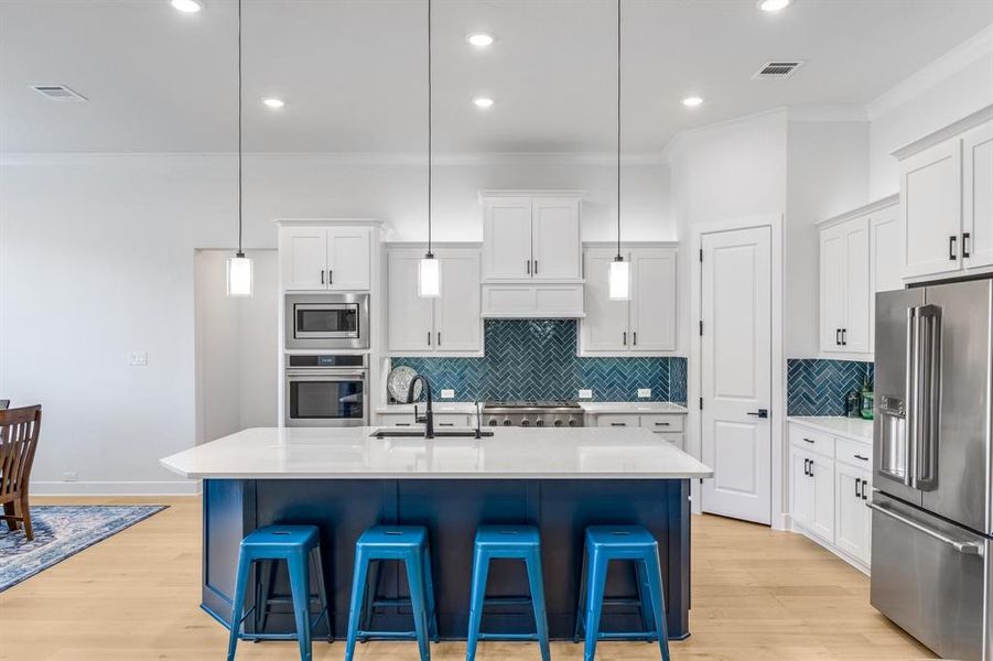 Kitchen with sink, decorative light fixtures, a kitchen island with sink, white cabinets, and appliances with stainless steel finishes