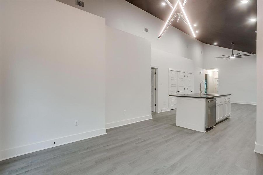 Kitchen with dark countertops, dishwasher, a center island with sink, open floor plan, and white cabinetry