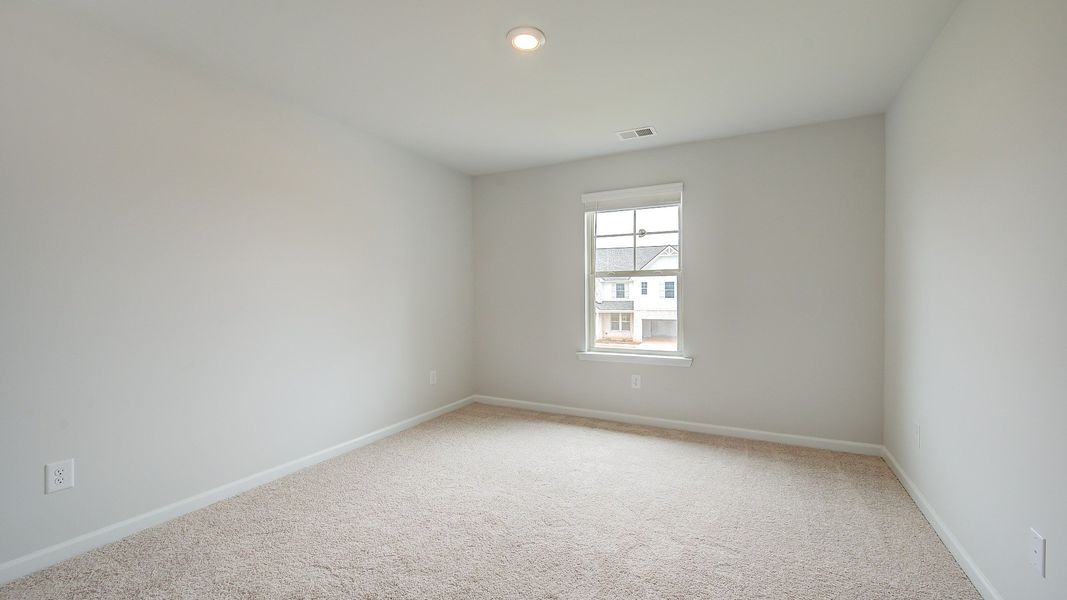 Secondary bedroom with carpet flooring and window providing natural light in the Meridian II at Brighton in Locust Grove, GA.