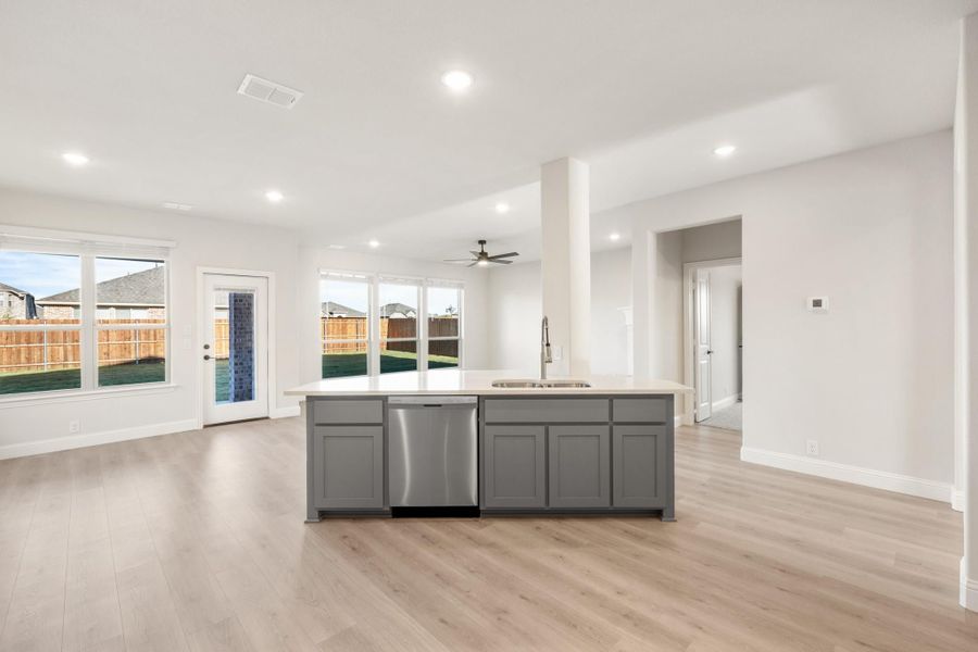 Open-concept kitchen with gray island, stainless dishwasher, and light wood floors overlooking backyard Open-concept kitchen with gray island, stainless dishwasher, and light wood floors overlooking backyard