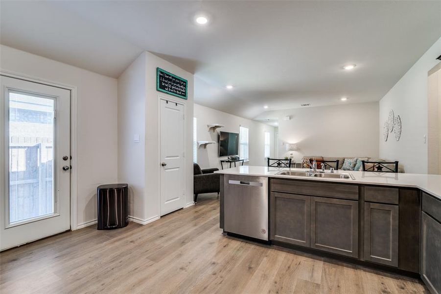 Kitchen with light wood-style flooring, a sink, open floor plan, light countertops, and stainless steel dishwasher