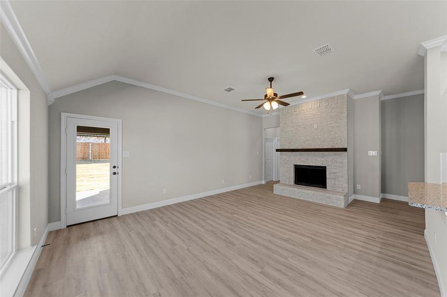 Unfurnished living room featuring light wood-style flooring, ornamental molding, ceiling fan, a large fireplace, and lofted ceiling