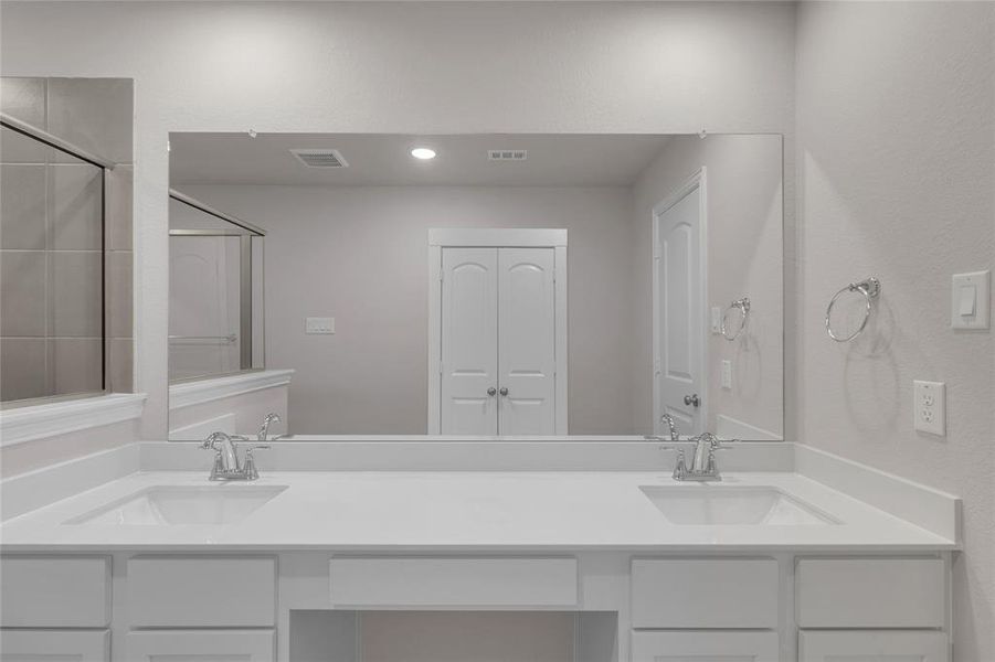 This photo shows a spacious primary bathroom with dual sinks, a large mirror, and ample cabinetry.