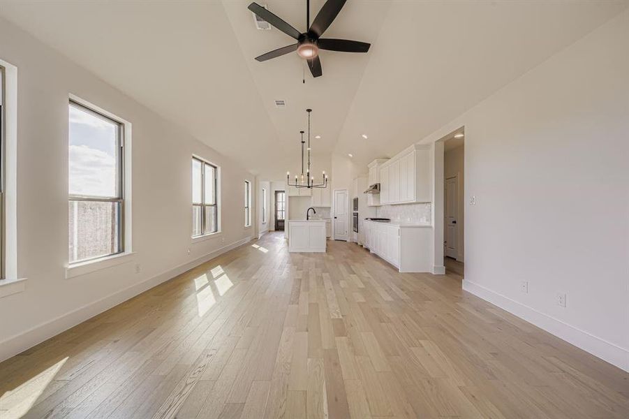 Unfurnished living room featuring light wood-type flooring, a chandelier, high vaulted ceiling, a ceiling fan, and recessed lighting Unfurnished living room featuring light wood-type flooring, a chandelier, high vaulted ceiling, a ceiling fan, and recessed lighting