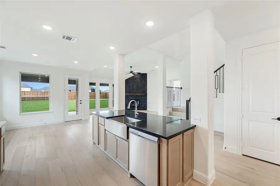 Kitchen island with dark countertop, farmhouse sink, and light wood cabinets open to living area with light hardwood floors