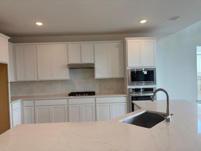 Kitchen featuring white cabinets, appliances with stainless steel finishes, light stone countertops, tasteful backsplash, and under cabinet range hood Kitchen featuring white cabinets, appliances with stainless steel finishes, light stone countertops, tasteful backsplash, and under cabinet range hood