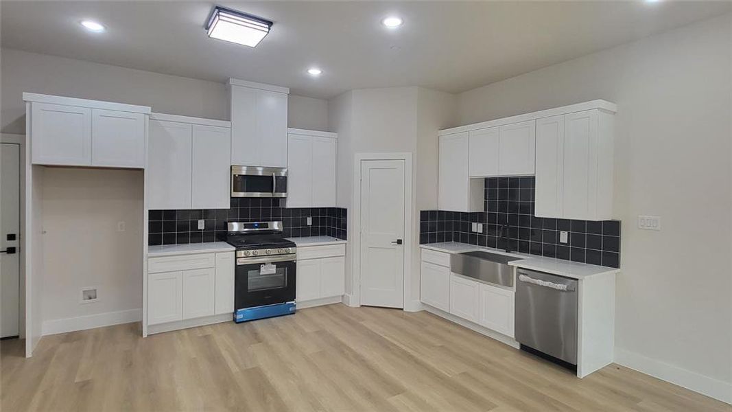 Kitchen featuring a sink, light wood-style flooring, stainless steel appliances, light countertops, and white cabinetry