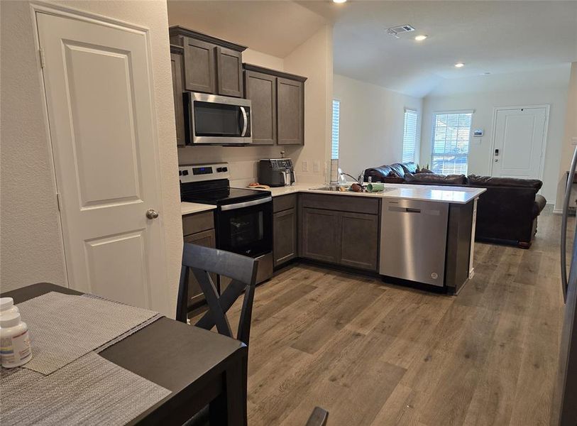 Kitchen featuring sink, dark brown cabinets, light hardwood / wood-style floors, kitchen peninsula, and stainless steel appliances