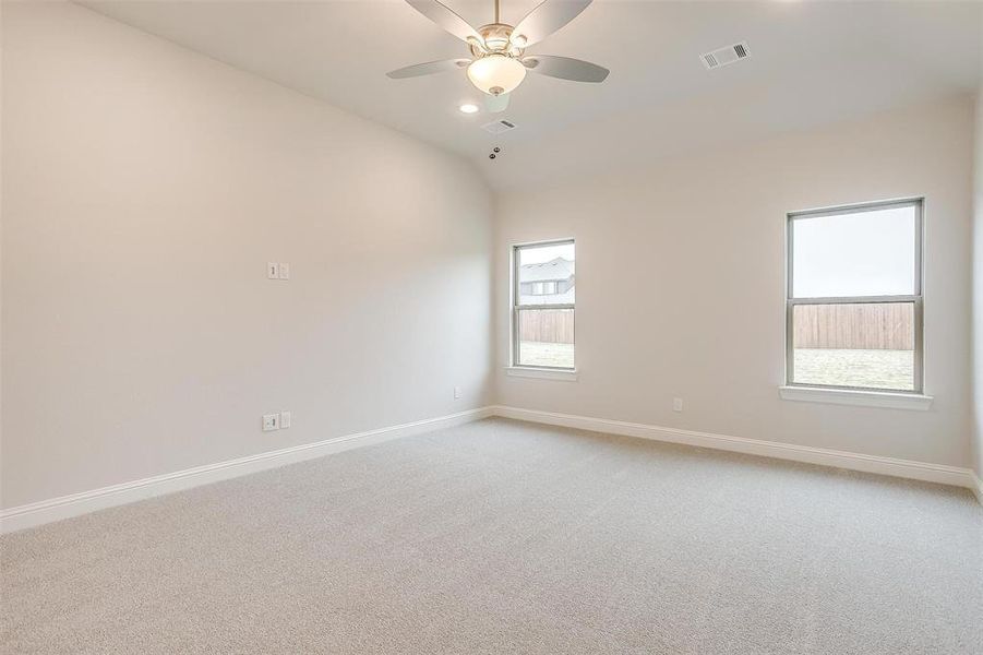 Carpeted spare room featuring a healthy amount of sunlight, vaulted ceiling, and ceiling fan