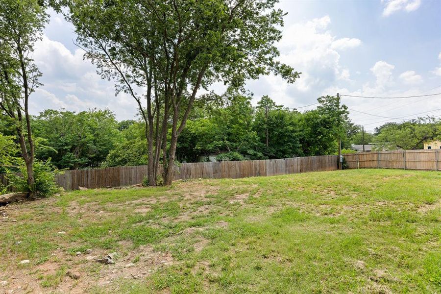 Expansive outdoor space featuring a wood privacy fence, mature trees, and a spacious lawn