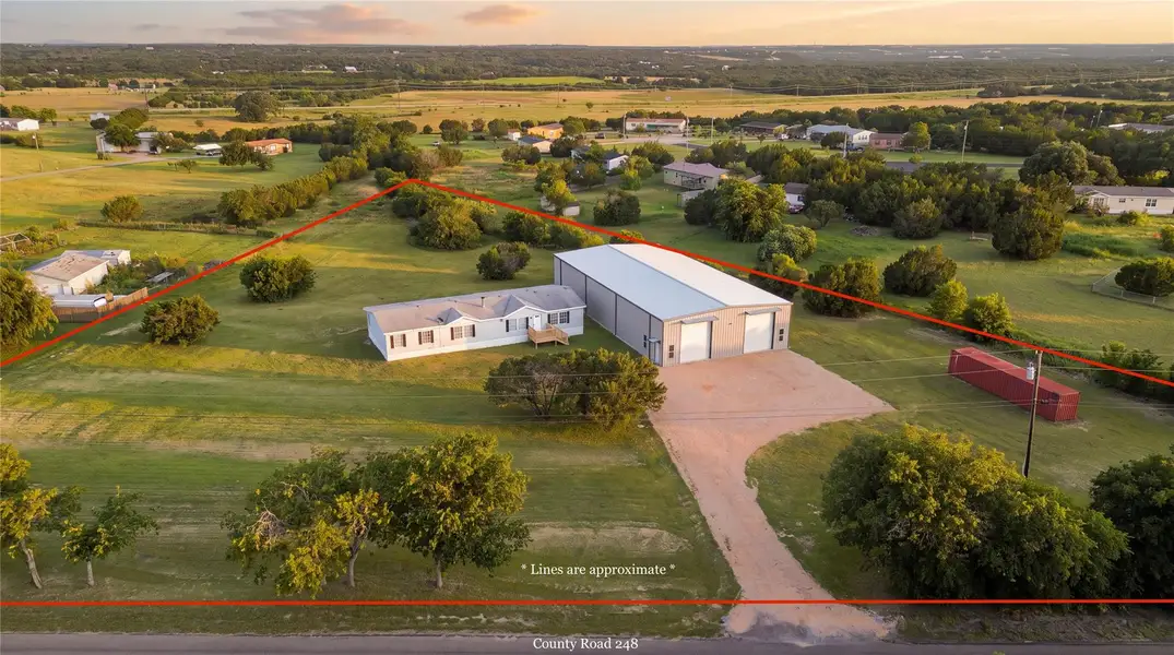 An expansive rural property features a manufactured home alongside a massive workshop on green acreage.