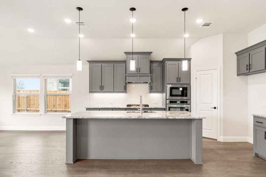 Kitchen with gray cabinets, large island with granite countertop, pendant lights, and stainless steel appliances Kitchen with gray cabinets, large island with granite countertop, pendant lights, and stainless steel appliances