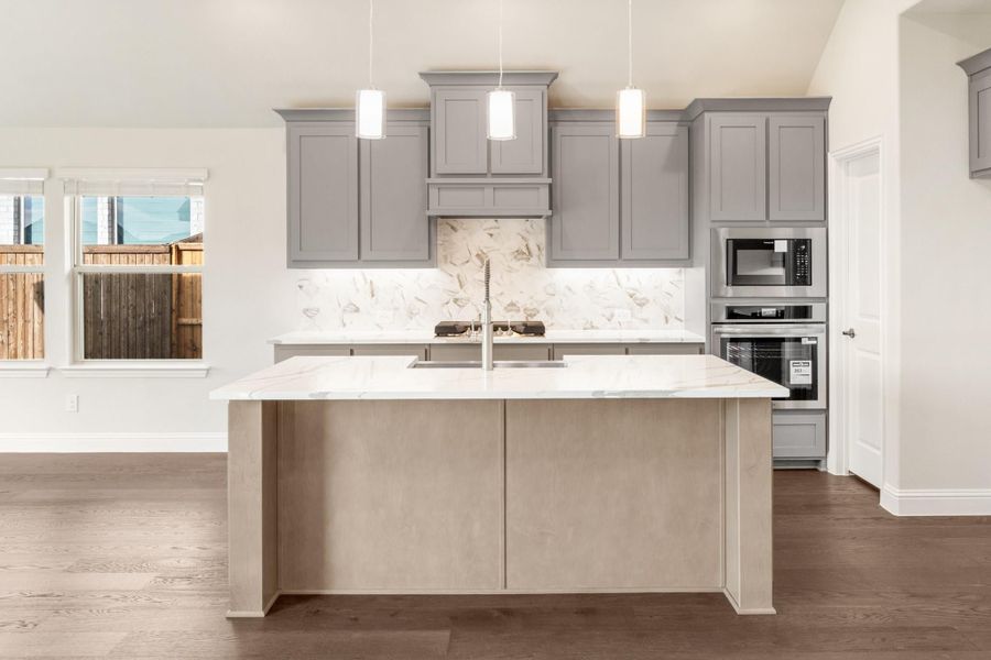 Kitchen with gray cabinets, marble backsplash, center island with sink, and built-in stainless steel appliances on hardwood floors Kitchen with gray cabinets, marble backsplash, center island with sink, and built-in stainless steel appliances on hardwood floors