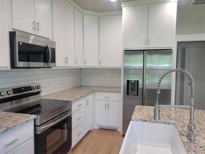 Modern kitchen featuring white shaker cabinetry, granite countertops, stainless steel appliances, subway tile backsplash, and a farmhouse-style sink with a pull-down faucet