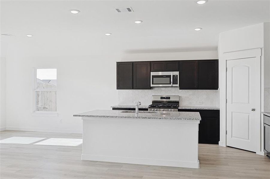 Kitchen with a center island with sink, light stone counters, sink, and stainless steel appliances