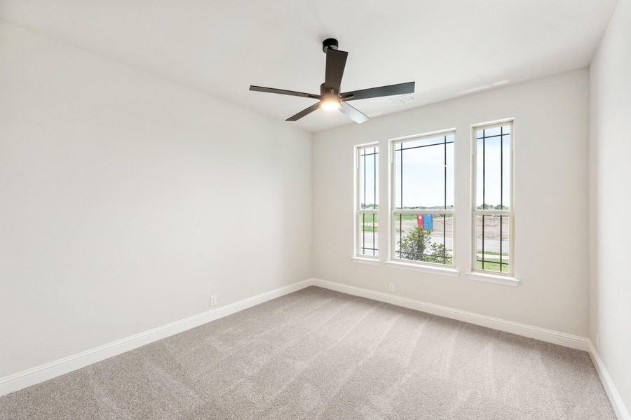 Empty bedroom with carpet flooring, black ceiling fan, and three windows with outdoor views Empty bedroom with carpet flooring, black ceiling fan, and three windows with outdoor views