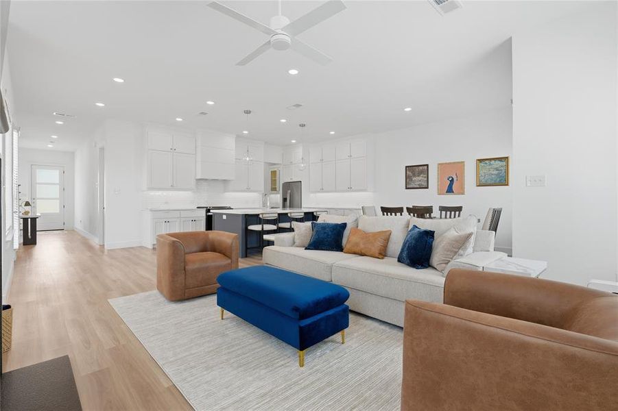 Open-concept living area featuring light wood-finish flooring, recessed lighting, a ceiling fan, and white walls