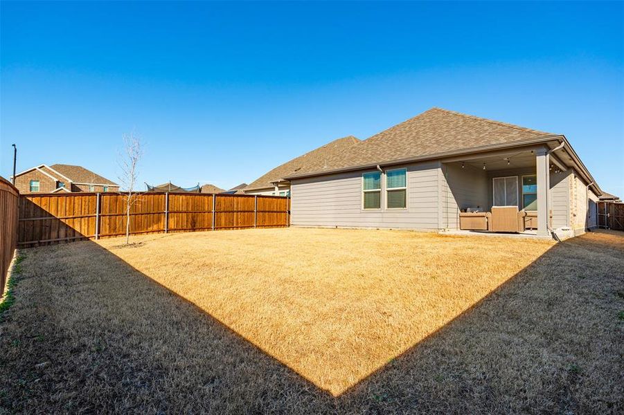 Rear view of house featuring a fenced backyard, a shingled roof, and a yard