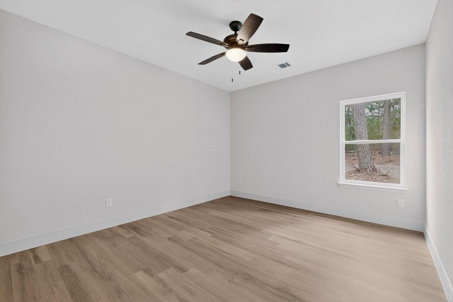 Room featuring light wood-finish flooring, a contemporary ceiling fan with integrated lighting, and a window framing a wooded backdrop Room featuring light wood-finish flooring, a contemporary ceiling fan with integrated lighting, and a window framing a wooded backdrop
