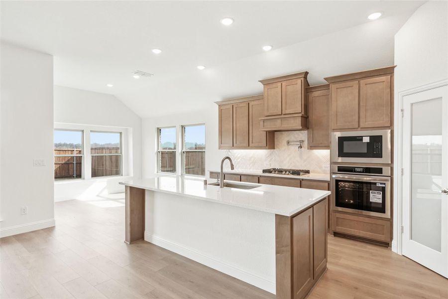 Kitchen with large center island, tan wood cabinets, white countertops, and stainless steel appliances Kitchen with large center island, tan wood cabinets, white countertops, and stainless steel appliances
