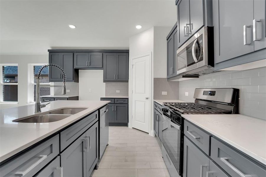 Kitchen featuring stainless steel appliances, light countertops, a sink, and decorative backsplash Kitchen featuring stainless steel appliances, light countertops, a sink, and decorative backsplash