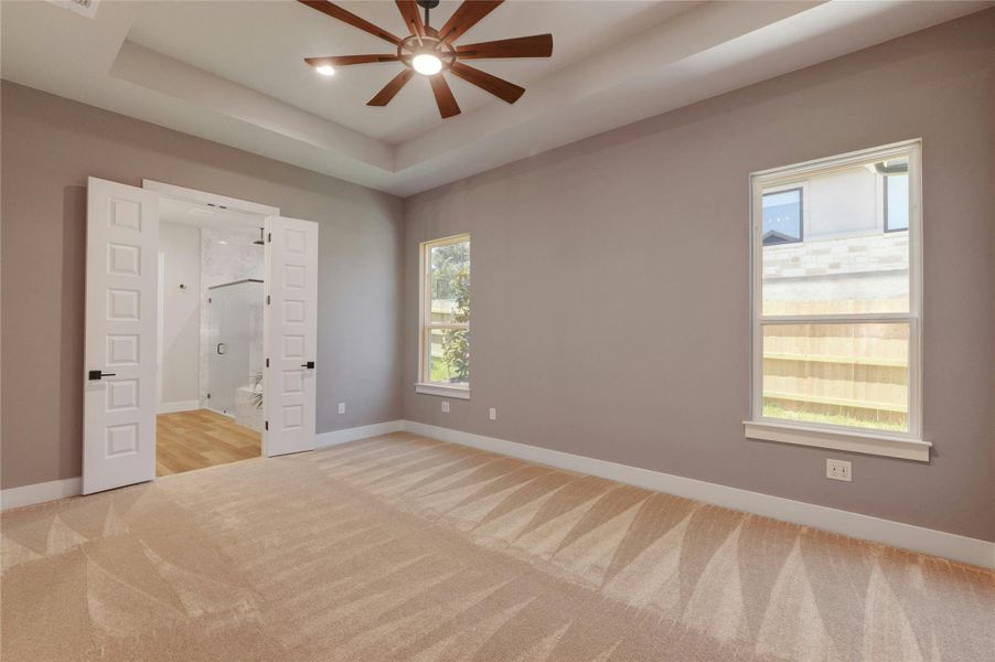 Spacious room with tray ceiling, modern ceiling fan, and carpeted flooring