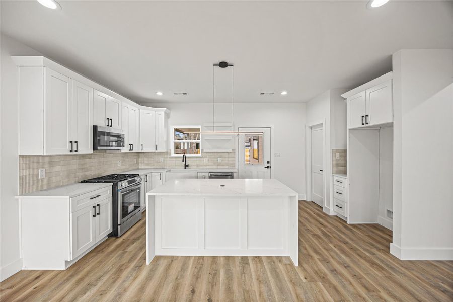 Modern kitchen featuring a large center island, quartz countertops, stainless steel appliances, and shaker-style cabinetry.