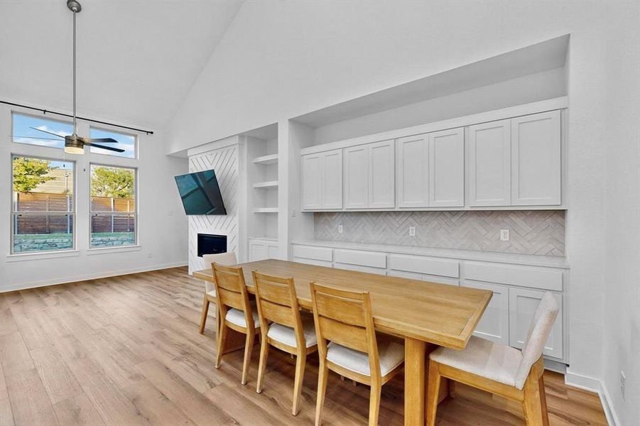Dining room featuring high vaulted ceiling, light wood-style flooring, a premium fireplace, built in features, and a ceiling fan Dining room featuring high vaulted ceiling, light wood-style flooring, a premium fireplace, built in features, and a ceiling fan