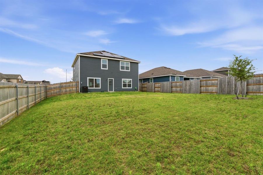 The property features a spacious backyard with a well-maintained lawn, enclosed by a wooden fence