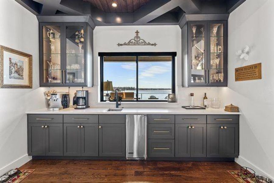 Indoor wet bar featuring glass insert cabinets, gray cabinetry, dark wood-style floors, and light stone counters