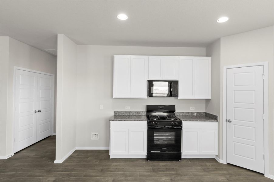 Kitchen with black appliances, dark wood-style flooring, white cabinets, recessed lighting, and dark stone counters Kitchen with black appliances, dark wood-style flooring, white cabinets, recessed lighting, and dark stone counters