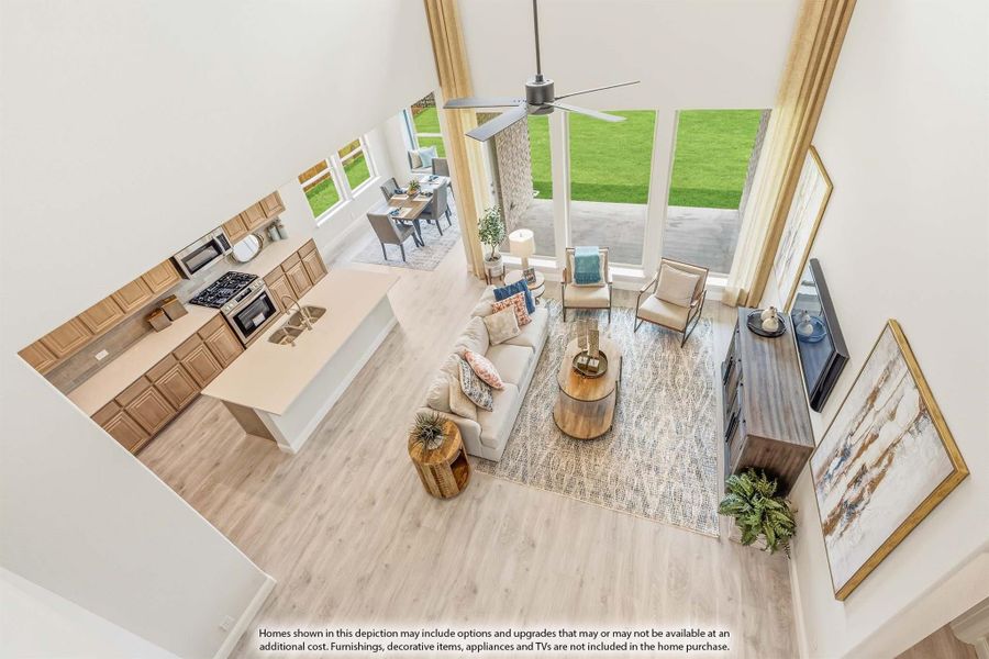 Open-concept living area and kitchen with two-story ceilings, hardwood floors, and large windows, viewed from above.