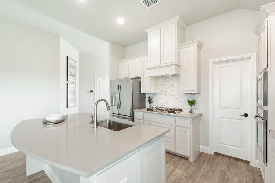 Kitchen with white cabinets, quartz island with sink, stainless steel appliances, and tile backsplash