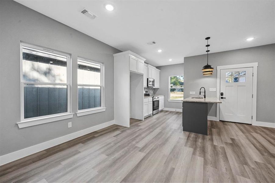 Kitchen featuring sink, white cabinets, hanging light fixtures, stainless steel appliances, and a center island with sink