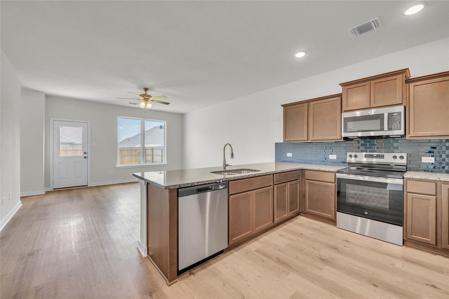 Kitchen featuring stainless steel appliances, decorative backsplash, light stone countertops, brown cabinetry, and a peninsula Kitchen featuring stainless steel appliances, decorative backsplash, light stone countertops, brown cabinetry, and a peninsula