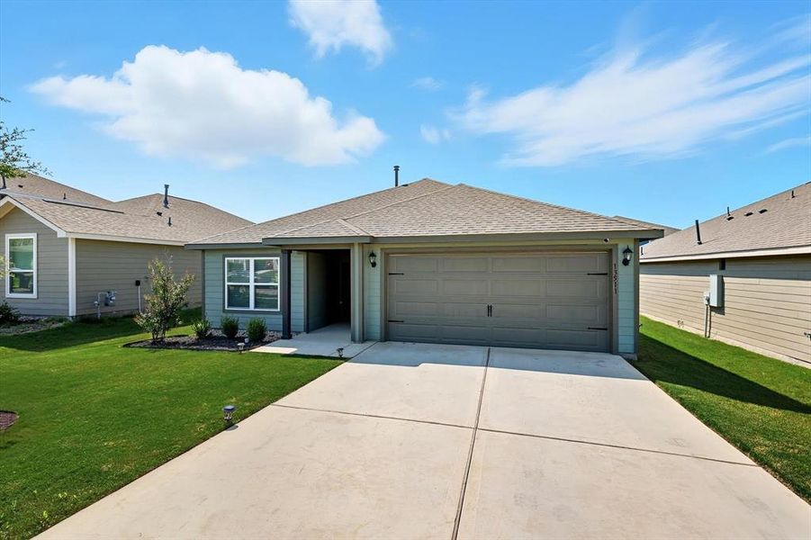 Single story home featuring roof with shingles, driveway, a front yard, and an attached garage