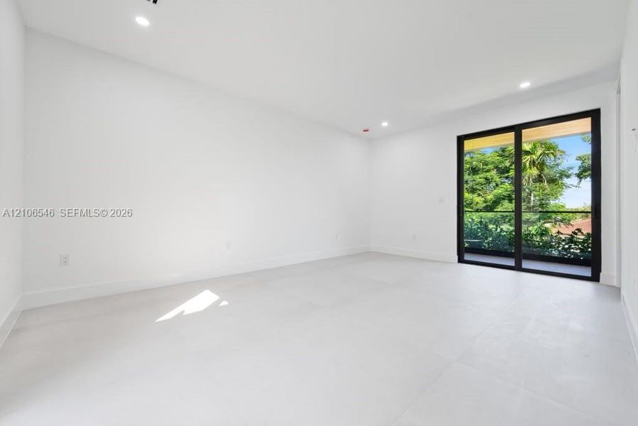 Interior space featuring large-format light-toned tile flooring, recessed ceiling lighting, and black-framed sliding glass doors opening to an exterior balcony