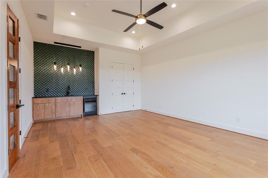 Spare room featuring a raised ceiling, light wood finished floors, recessed lighting, a ceiling fan, and bar with sink