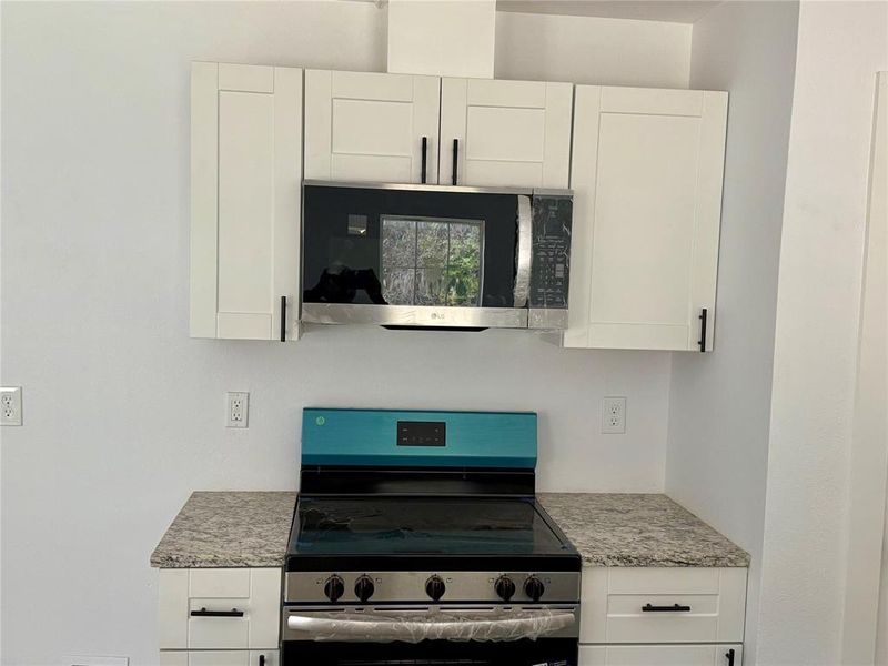 Kitchen featuring appliances with stainless steel finishes, white cabinetry, and light stone countertops