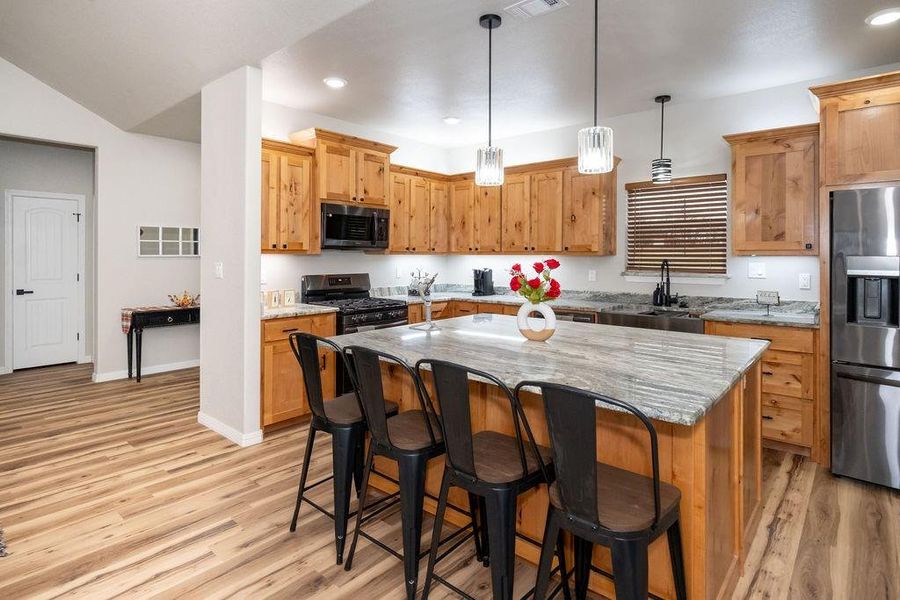 Kitchen with appliances with stainless steel finishes, decorative light fixtures, sink, a center island, and light stone countertops