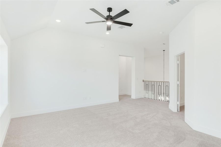 Open upstairs bonus room with vaulted ceiling, ceiling fan, carpet flooring, and metal stair railing.