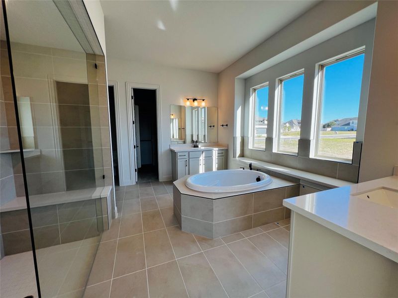 Full bathroom with light tile patterned flooring, a bath, two vanities, and a tile shower