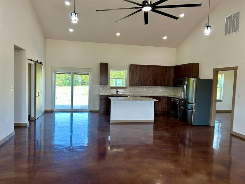 Kitchen with dark brown cabinets, high vaulted ceiling, a barn door, backsplash, and stainless steel refrigerator with ice dispenser
