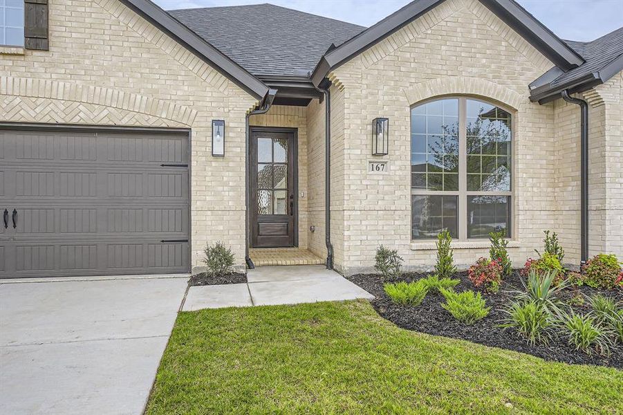 Entrance to property featuring roof with shingles, brick siding, and an attached garage