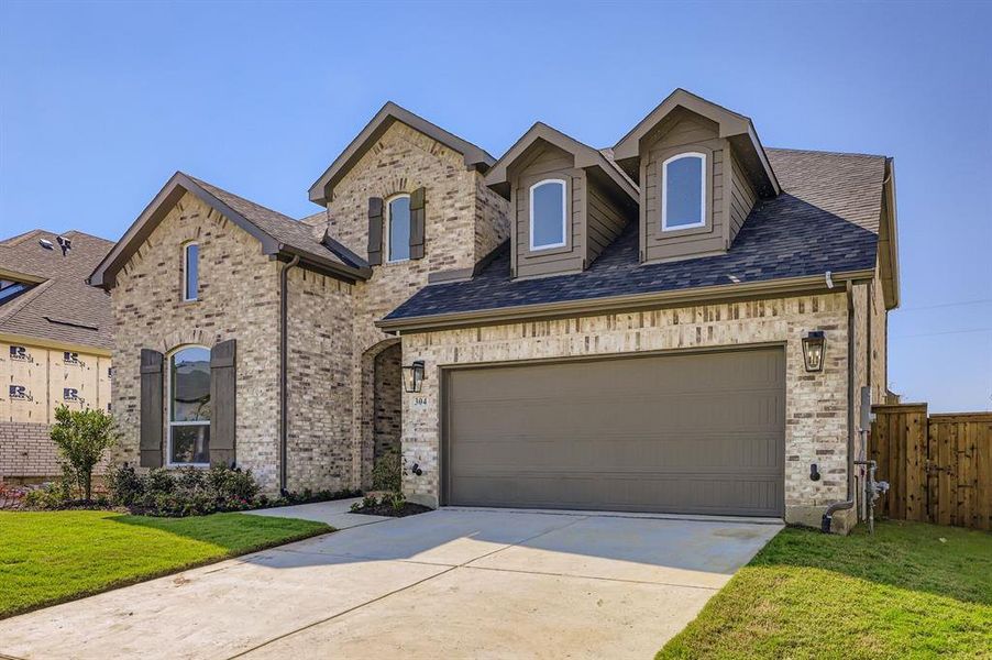 French country inspired facade featuring driveway, a garage, a shingled roof, and brick siding French country inspired facade featuring driveway, a garage, a shingled roof, and brick siding