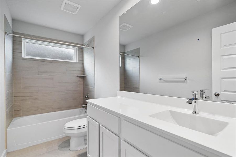 Secondary bath features tile flooring, bath/shower combo with tile surround, white stained wood cabinets, beautiful light countertops, mirror, sleek fixtures and modern finishes.